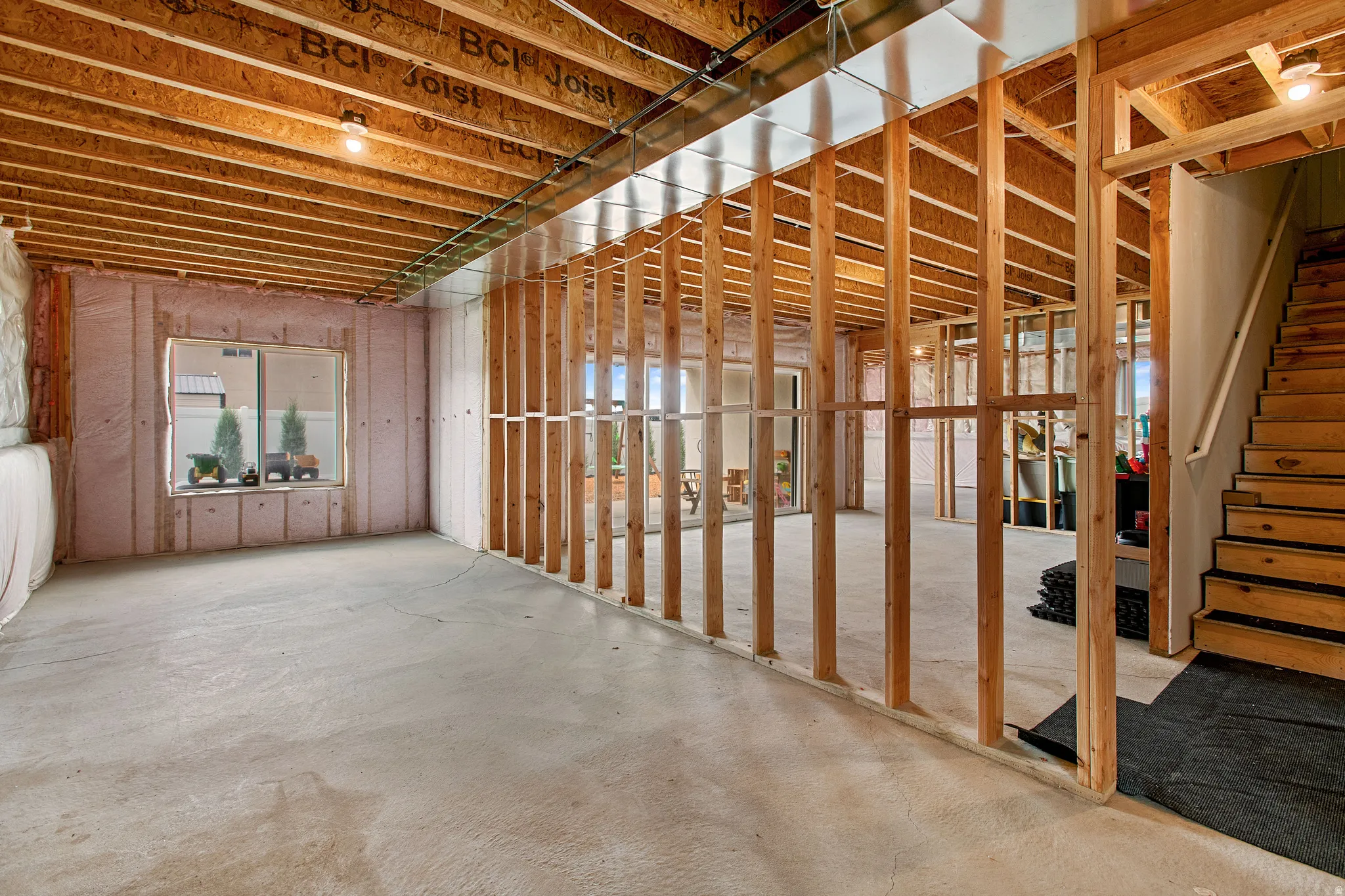 Unfinished basement with exposed wood framing, concrete flooring, and an egress window