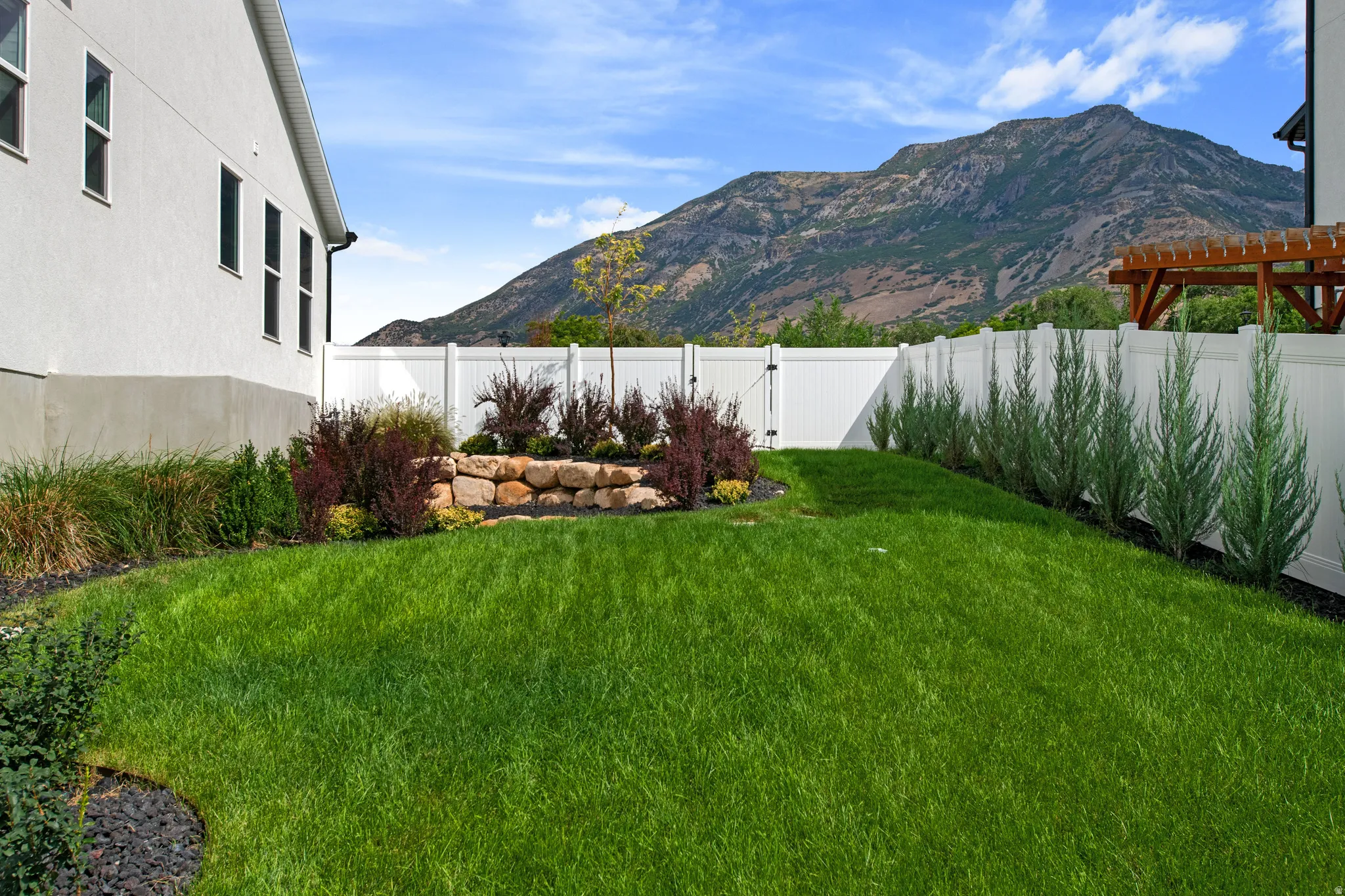 Expansive lawn area with a white privacy fence, stone retaining wall, and mature landscaping