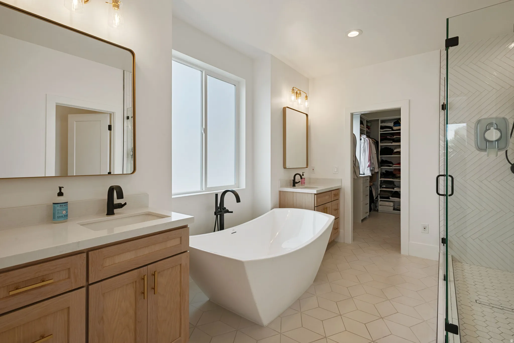 Freestanding soaking tub, dual vanities with quartz countertops, walk-in shower with herringbone tile, and a walk-in closet with custom shelving