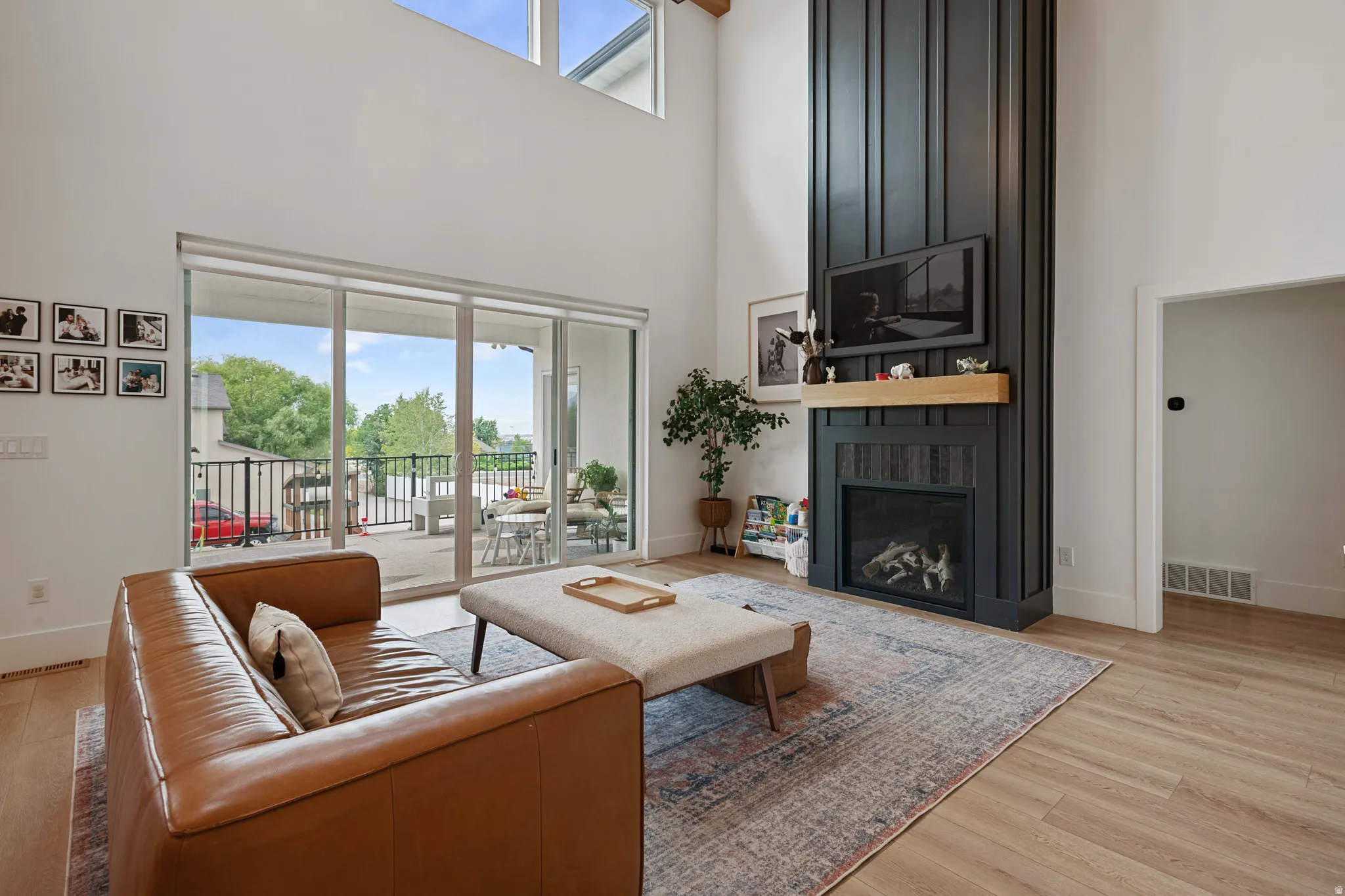 Double-height ceiling, floor-to-ceiling fireplace with wood mantel, large sliding glass doors, upper windows, and wood-finish flooring