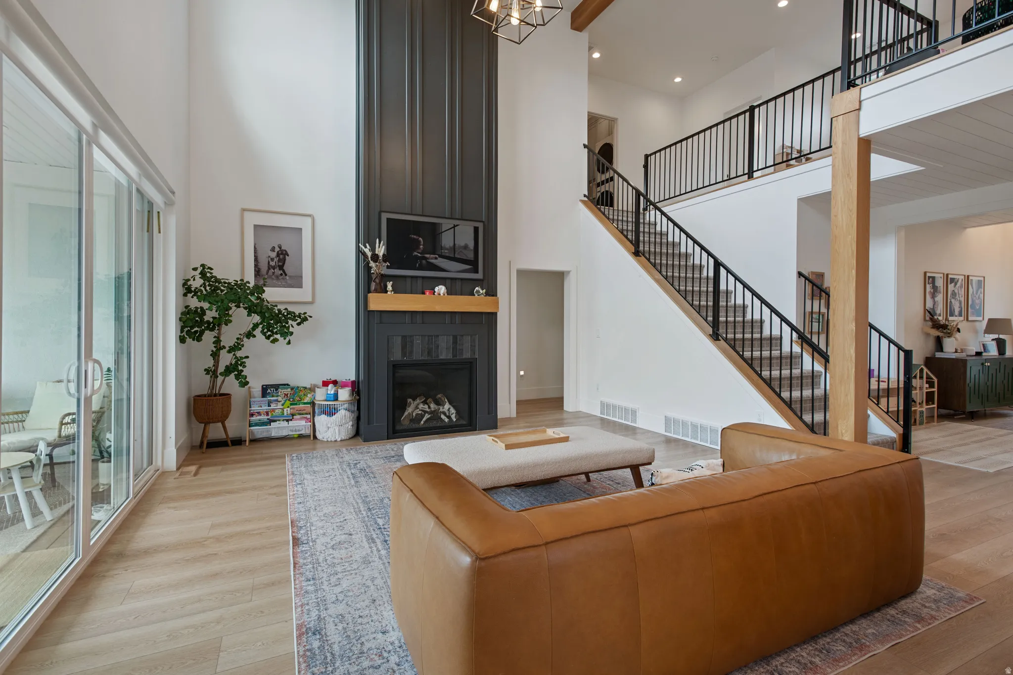 Two-story living area featuring a fireplace with a wood mantel, high ceilings, large sliding glass doors, and wood-finish flooring