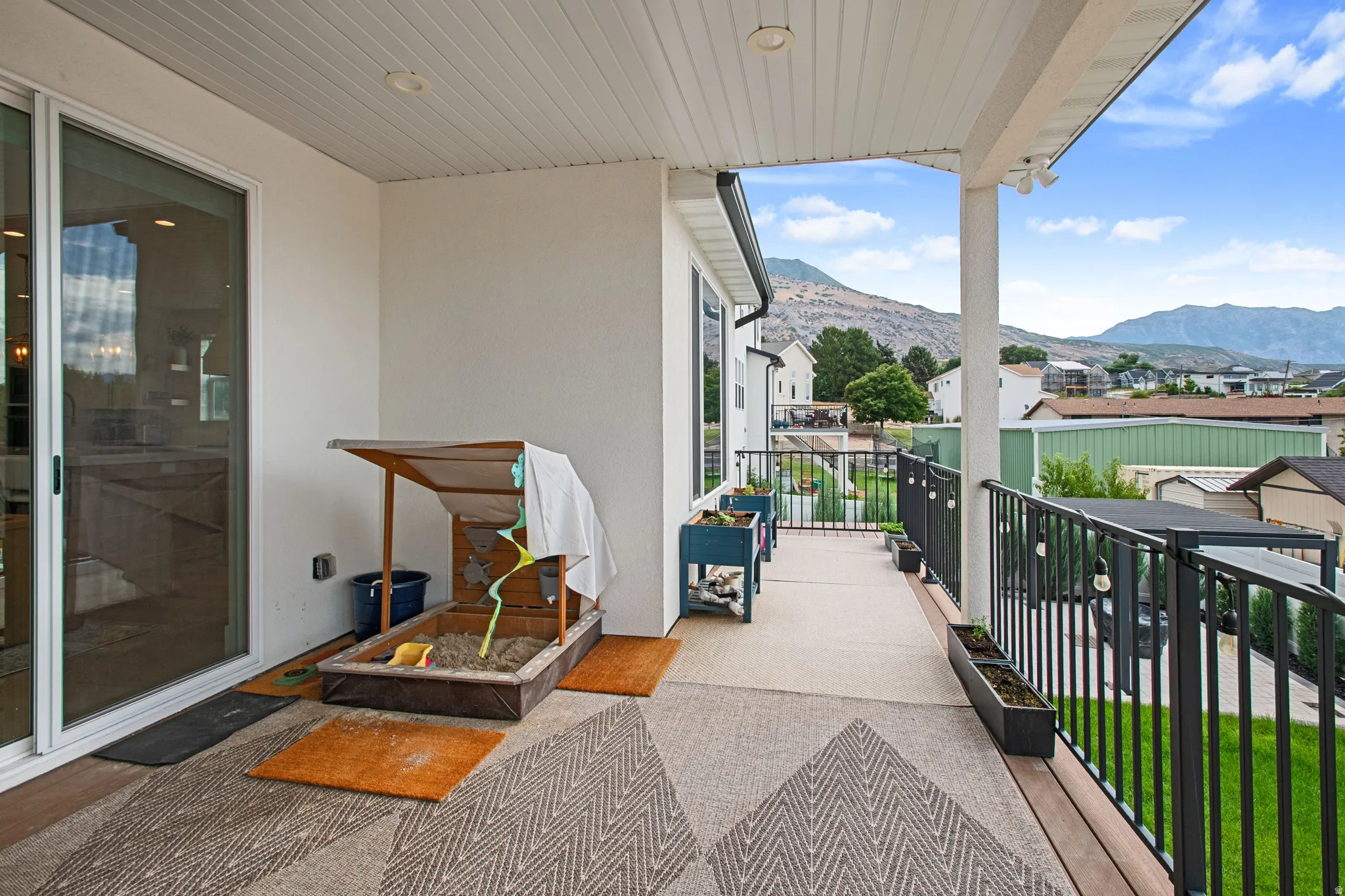 Expansive outdoor balcony featuring a sliding glass door, white paneled ceiling, and black metal railings