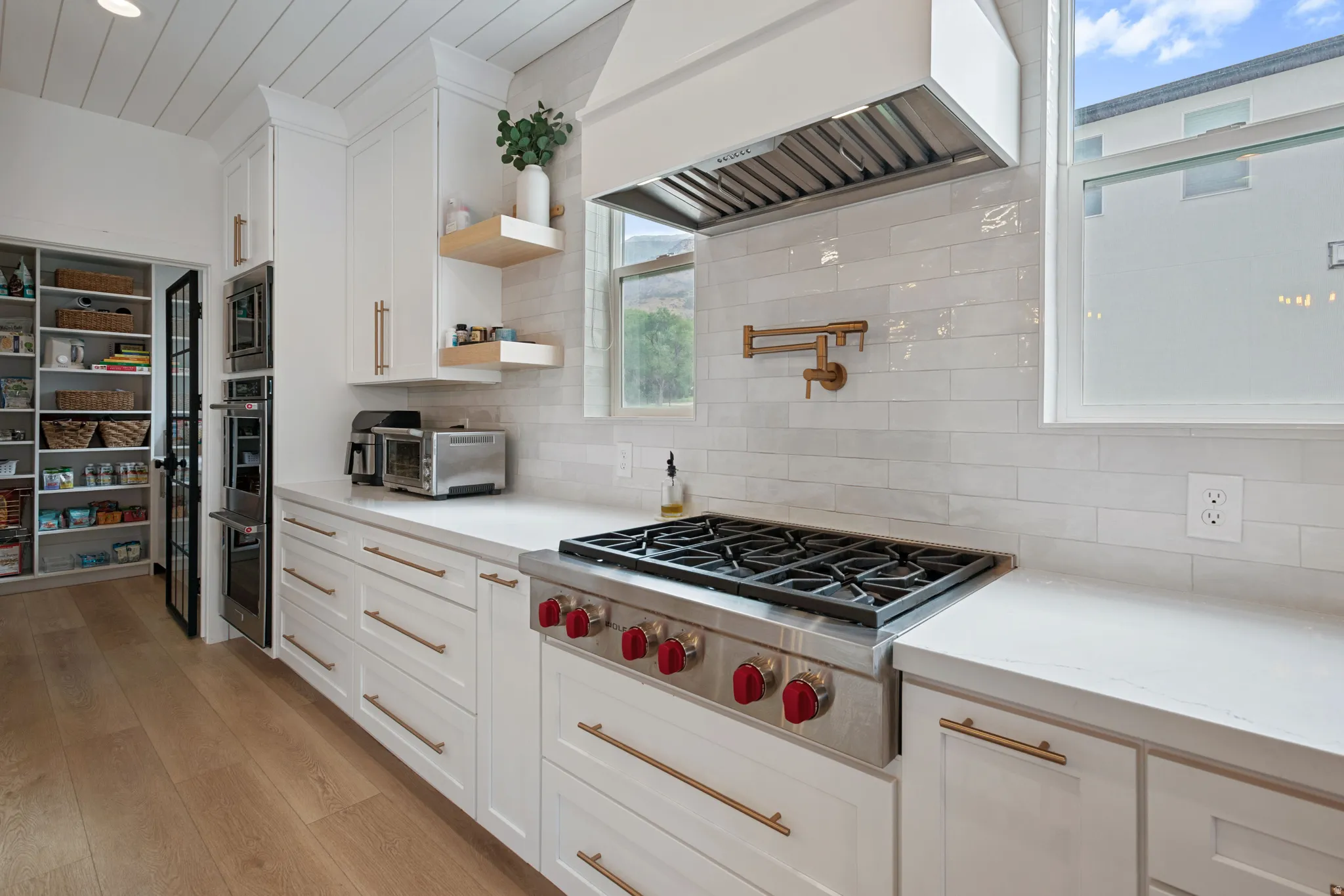 White cabinetry with gold-tone hardware, wood-finish flooring, and built-in stainless steel appliances
