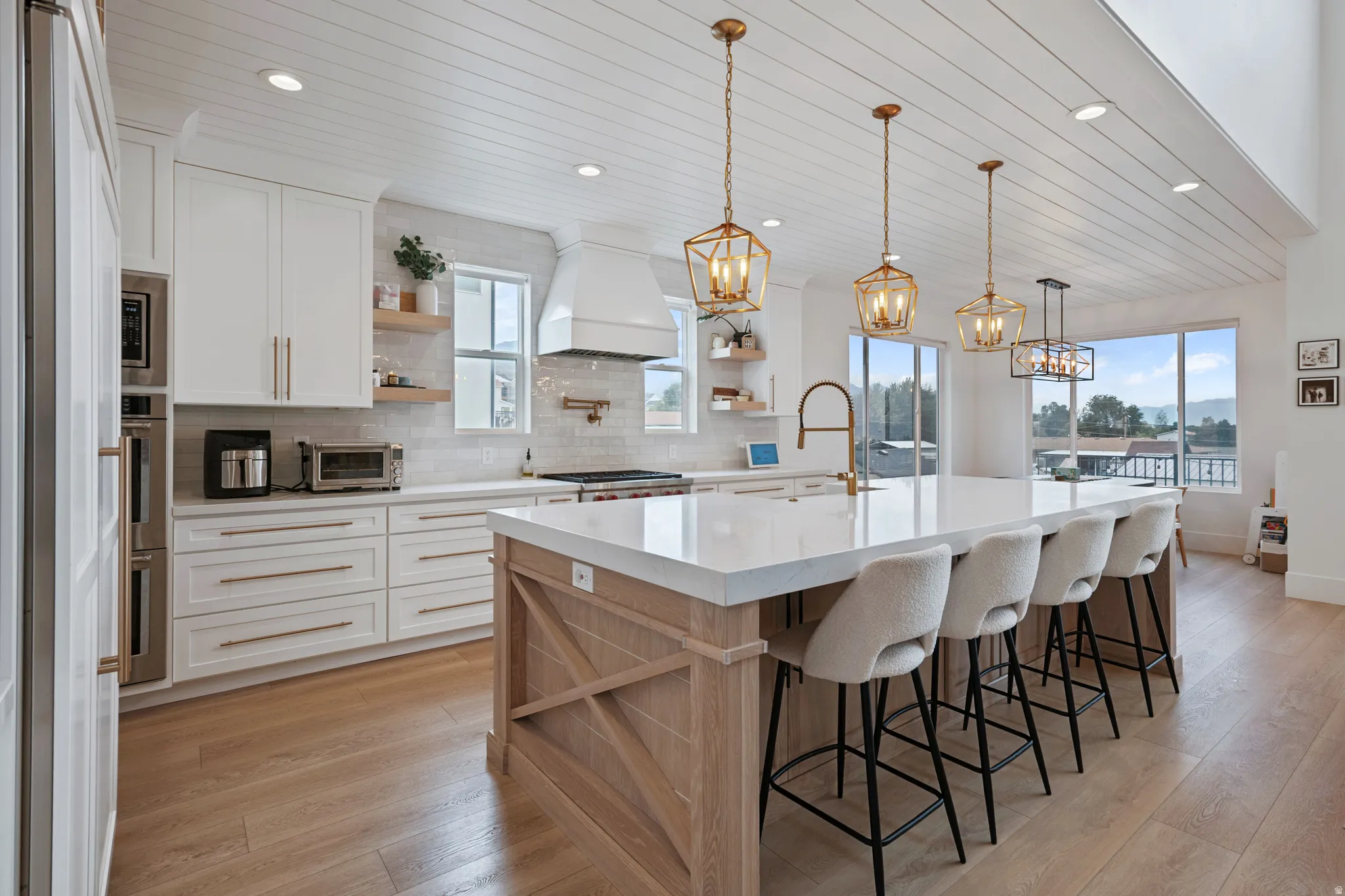 Spacious kitchen featuring white cabinetry, a large center island with seating, pendant lighting, built-in stainless steel appliances, and wood-finish flooring