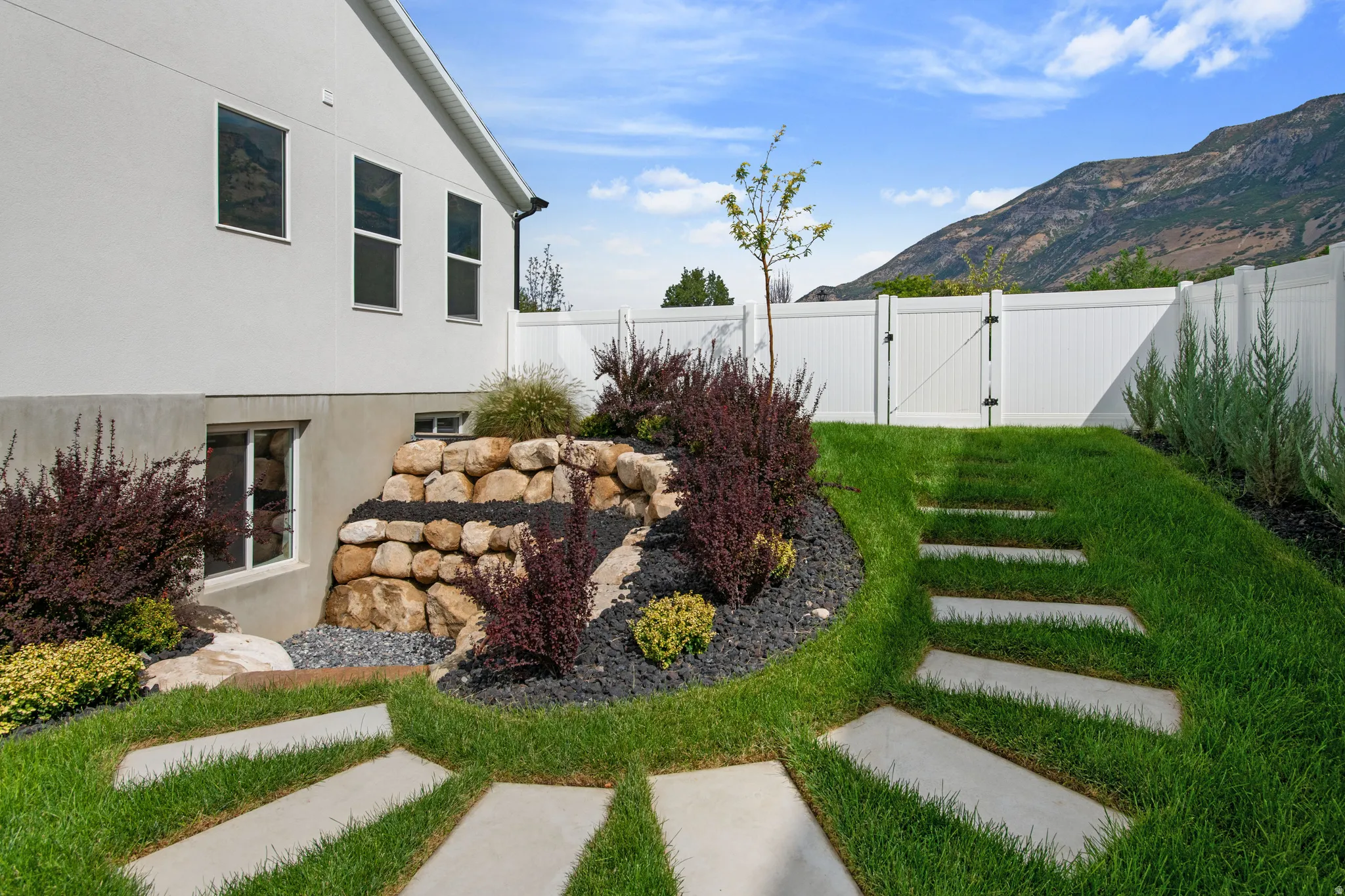 Lush green lawn with integrated concrete stepping stones, a tiered rock landscaping feature, and a privacy fence with a gated entry