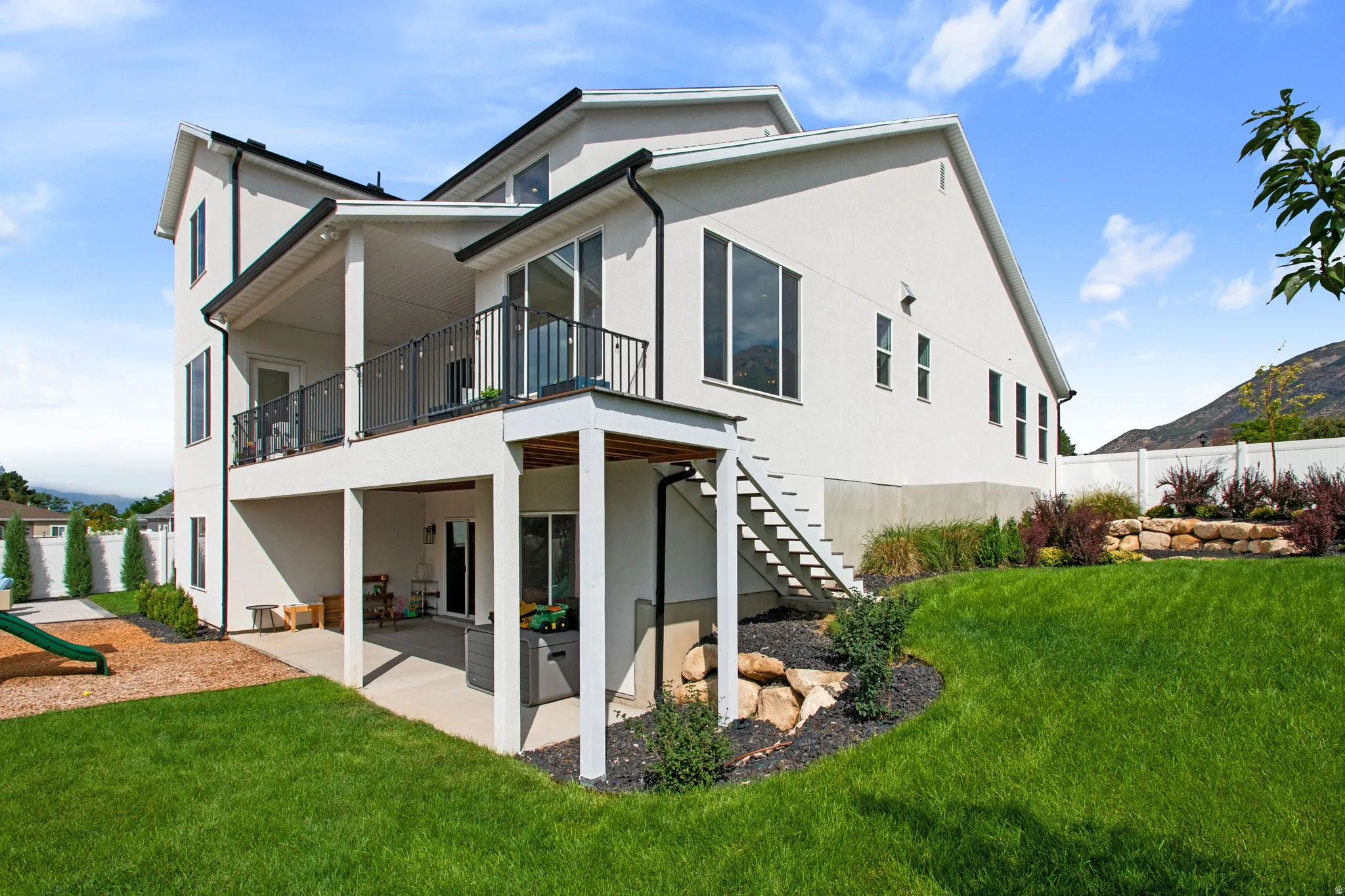 Multi-level exterior with a covered upper balcony, covered lower patio, and a staircase providing direct access to the yard
