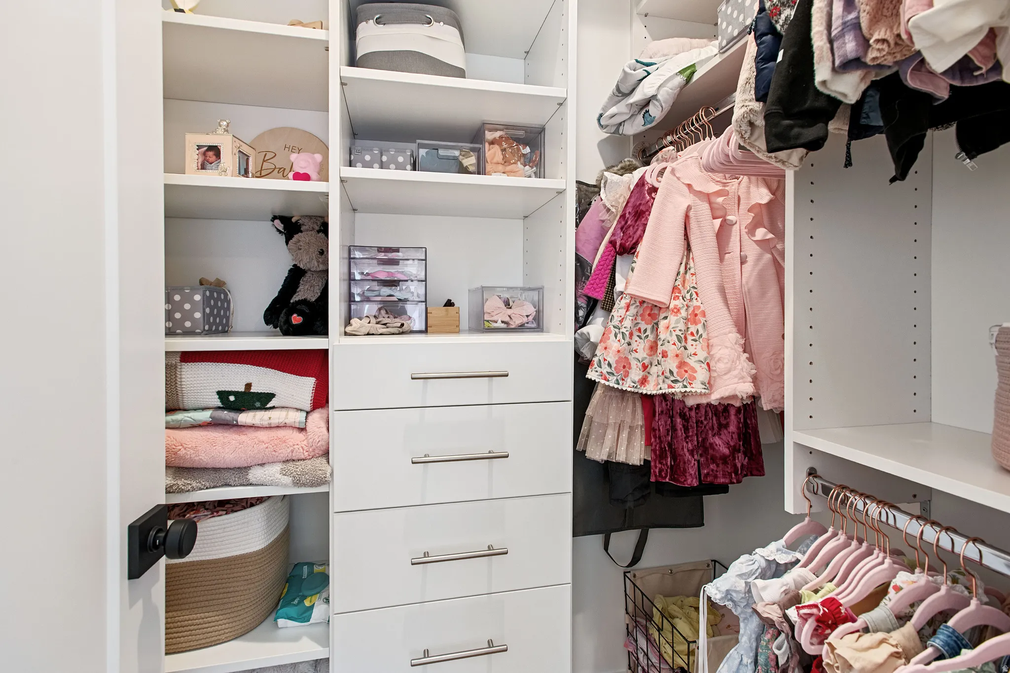 Built-in white custom closet system featuring multiple shelving units, integrated drawers with stainless steel pulls, and dedicated hanging rods