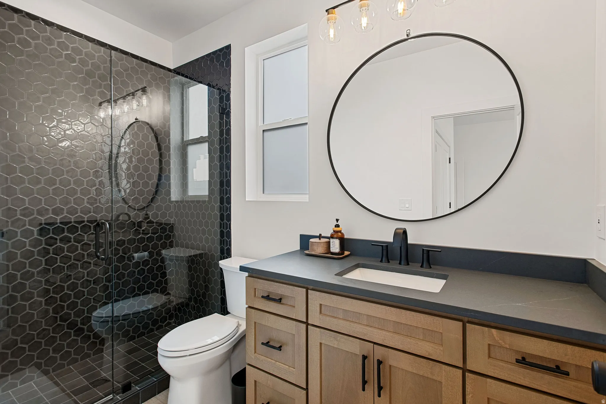 Modern bathroom featuring a wood-finish vanity, dark countertop with integrated sink, and black fixtures