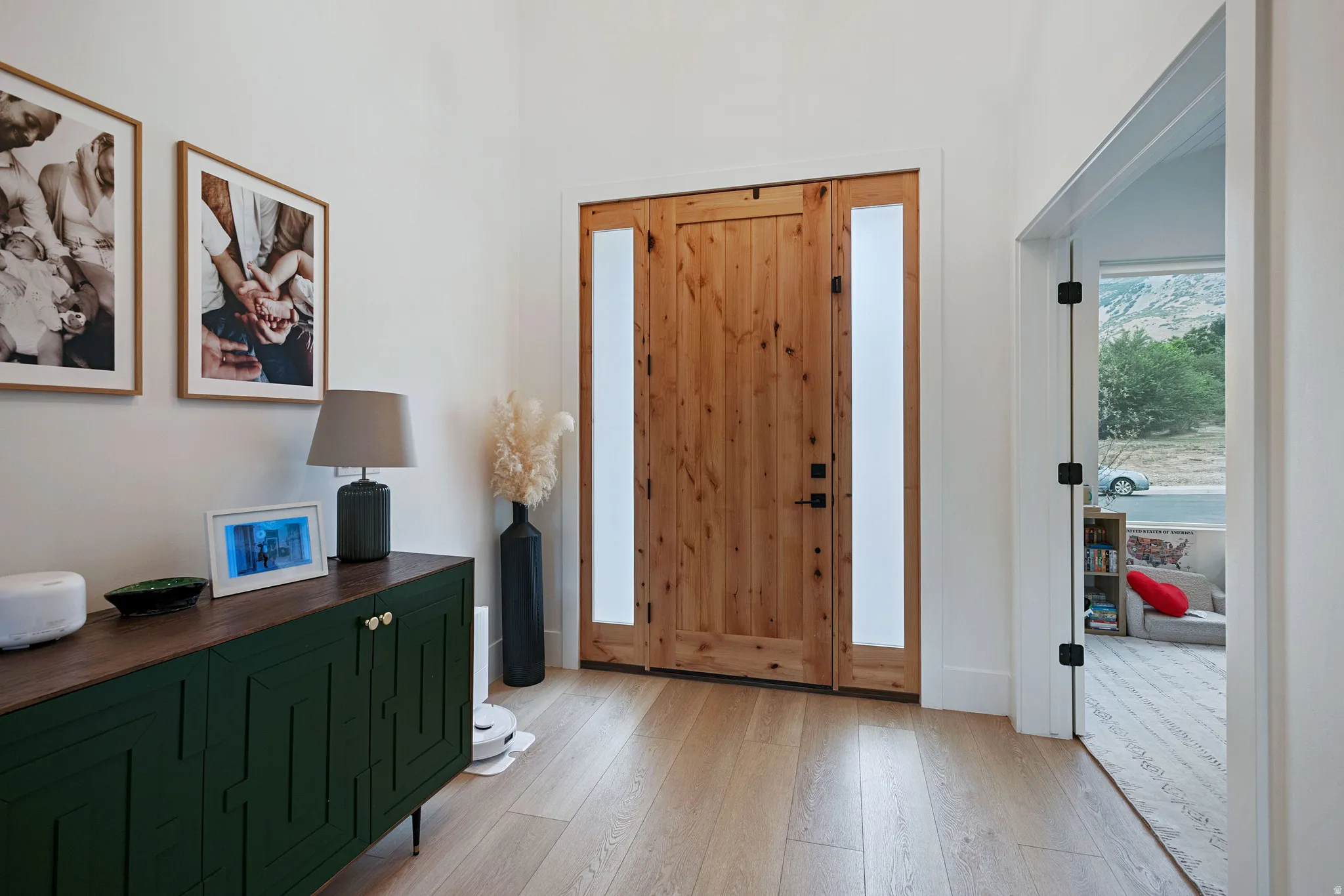 Natural wood-finish flooring, solid wood entry door with frosted side panels, and recessed wall paneling