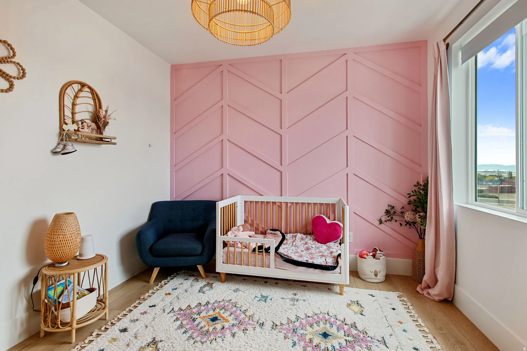 Pink accent wall with chevron paneling, light wood-finish flooring, and a rattan-style ceiling fixture
