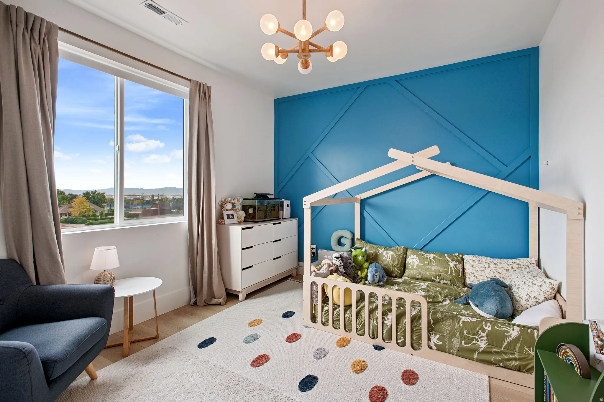 Expansive window with natural light, wood-finish flooring, accent wall with geometric paneling, and a contemporary ceiling fixture