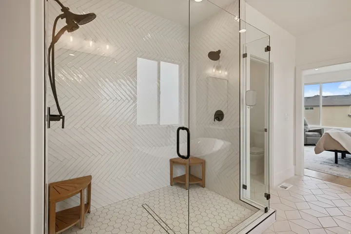Glass-enclosed shower with a dark bronze rainfall shower head, herringbone tile shower surround, hexagon tile flooring, and a linear drain