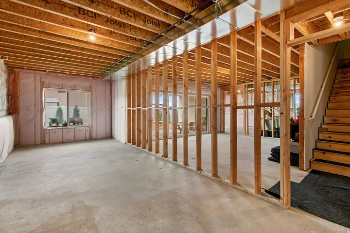 Unfinished basement with exposed wood framing, concrete flooring, and an egress window