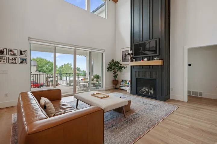 Double-height ceiling, floor-to-ceiling fireplace with wood mantel, large sliding glass doors, upper windows, and wood-finish flooring