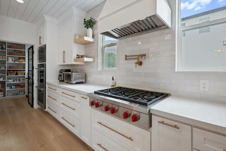 White cabinetry with gold-tone hardware, wood-finish flooring, and built-in stainless steel appliances