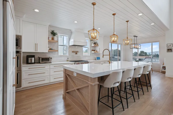 Spacious kitchen featuring white cabinetry, a large center island with seating, pendant lighting, built-in stainless steel appliances, and wood-finish flooring