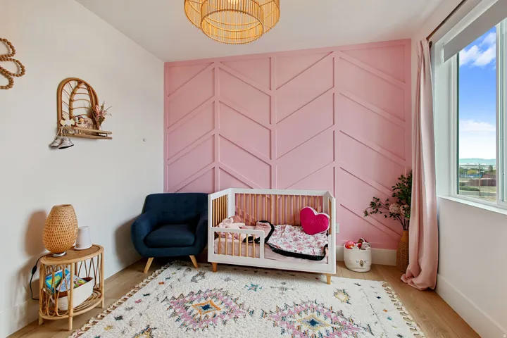 Pink accent wall with chevron paneling, light wood-finish flooring, and a rattan-style ceiling fixture