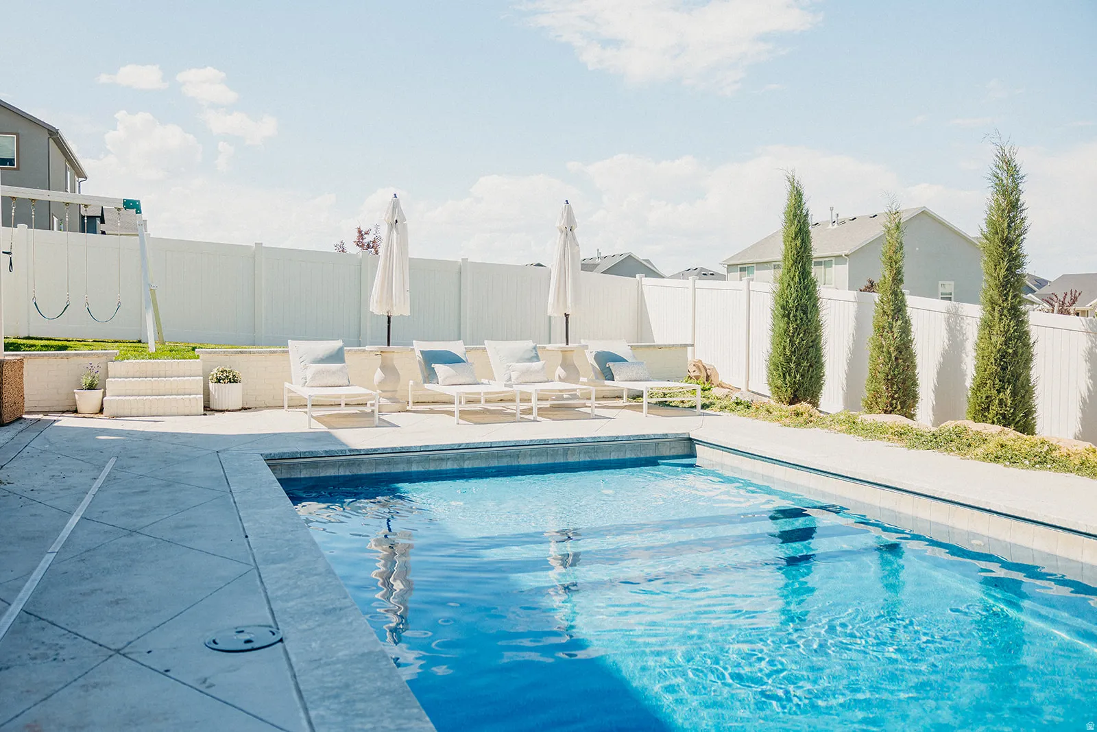 In-ground swimming pool with integrated steps, concrete surround, and perimeter landscaping