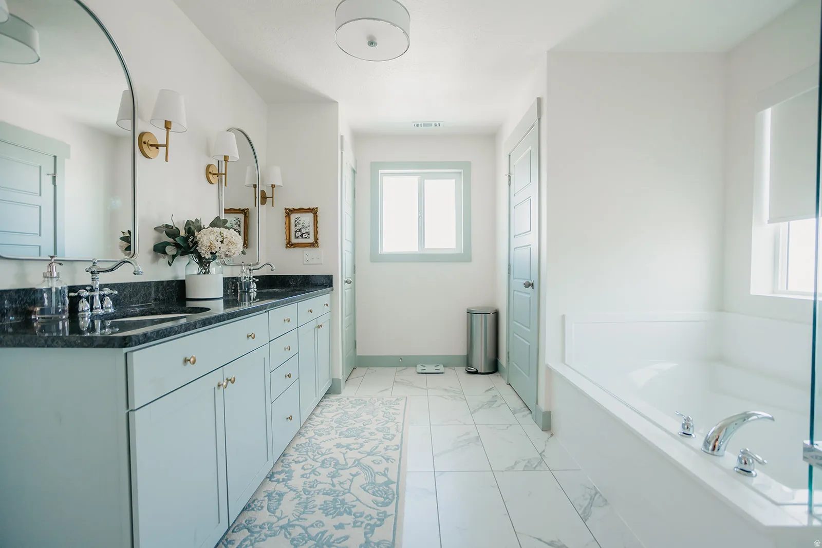 Double vanity with dark countertops and undermount sinks, flanked by arched mirrors with wall-mounted sconces