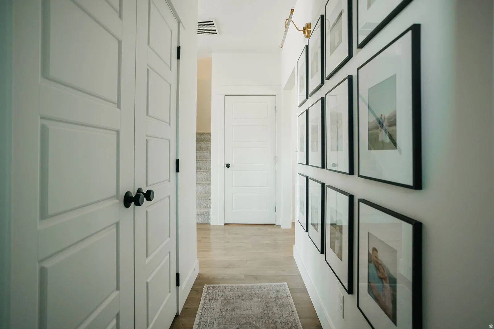 White paneled doors with matte black hardware, wood-finish flooring, and a wall-mounted light fixture