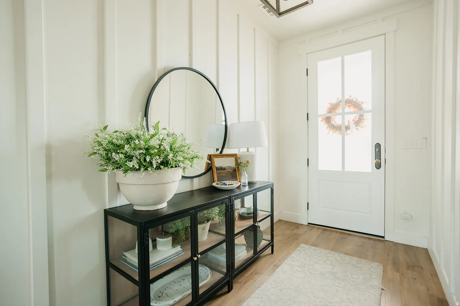 Vertical shiplap wall paneling, wood-finish flooring, white paneled door with glass inserts, and a contemporary ceiling-mounted light fixture