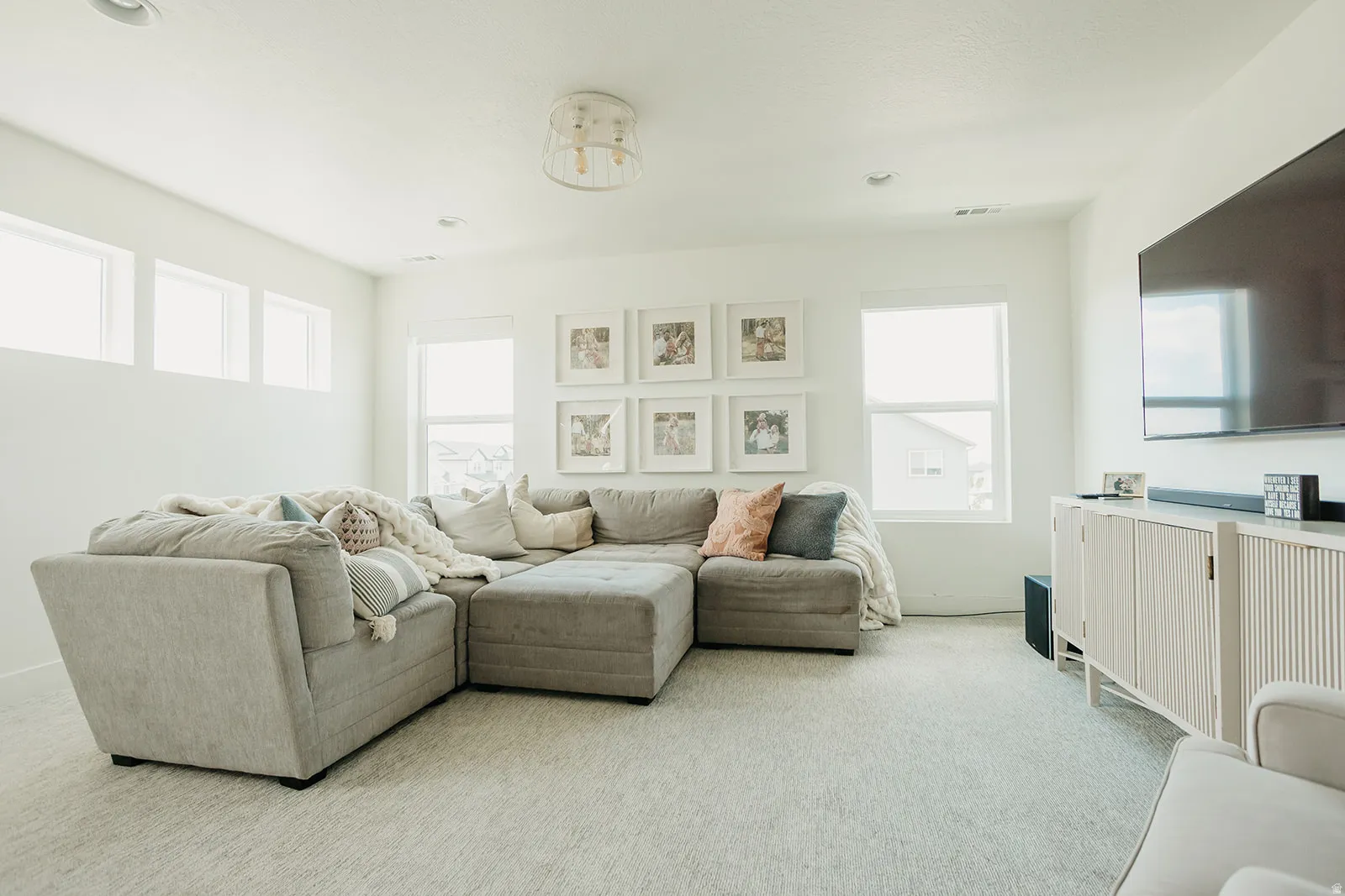 Recessed lighting, three high transom windows, a large window, and a built-in entertainment console with slatted doors