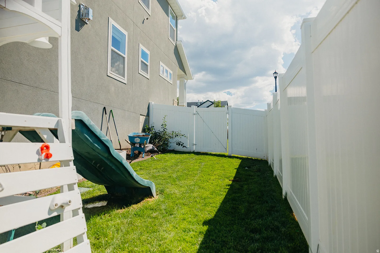 Manicured lawn with white vinyl fencing and a side gate, complemented by a stucco exterior and white-framed windows