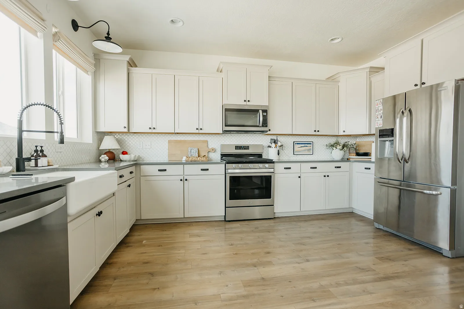 White cabinetry with dark hardware, stainless steel appliances, wood-finish flooring, apron-front sink, and a tiled backsplash