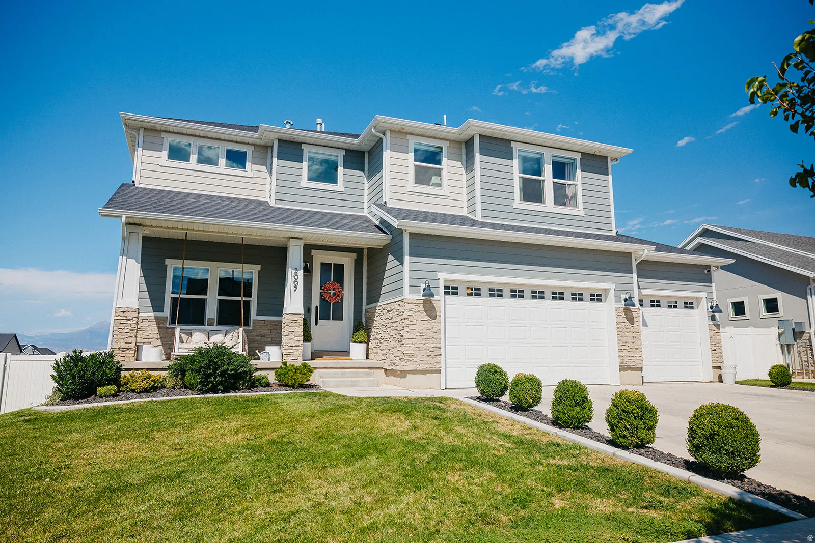 Two-story residence featuring light blue and white siding, stone veneer accents, and multiple windows