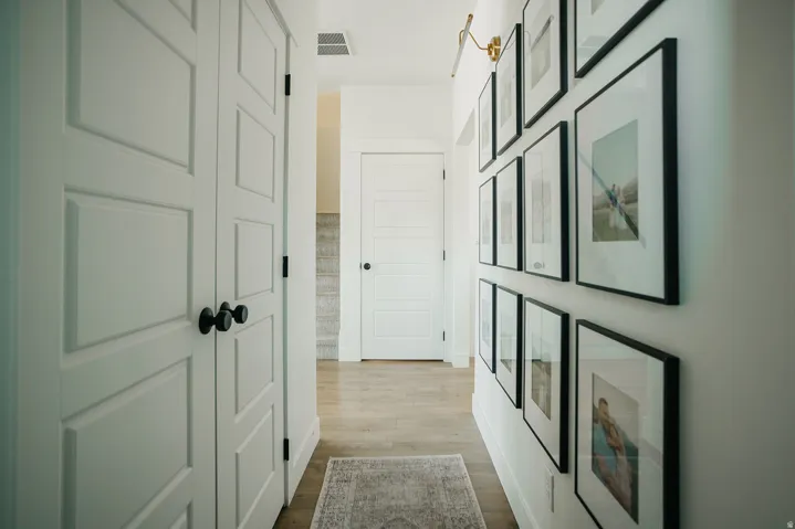 White paneled doors with matte black hardware, wood-finish flooring, and a wall-mounted light fixture
