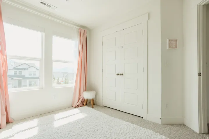 Bright interior space featuring dual windows, white trim work, and a closet with bifold doors