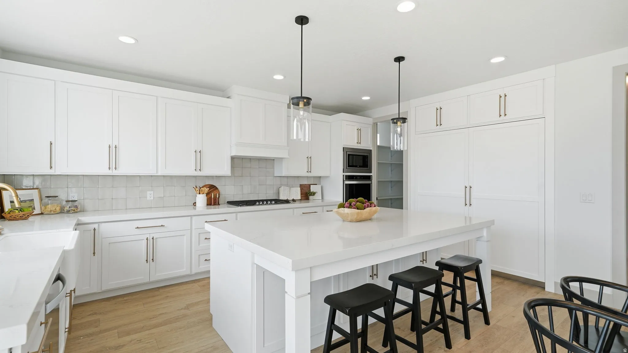 White cabinetry with coordinating countertops, light wood-finish flooring, integrated appliances, a built-in oven, and a central island with pendant lighting