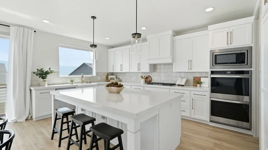 White shaker cabinetry, light-toned wood-finish flooring, recessed lighting, and stainless steel appliances including a built-in microwave and double ovens