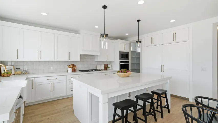 White cabinetry with coordinating countertops, light wood-finish flooring, integrated appliances, a built-in oven, and a central island with pendant lighting