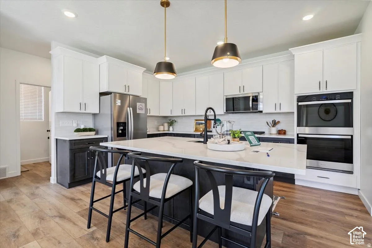 Kitchen featuring white upper cabinetry, dark lower cabinetry, a center island with a light-toned countertop, stainless steel appliances, and wood-finish flooring