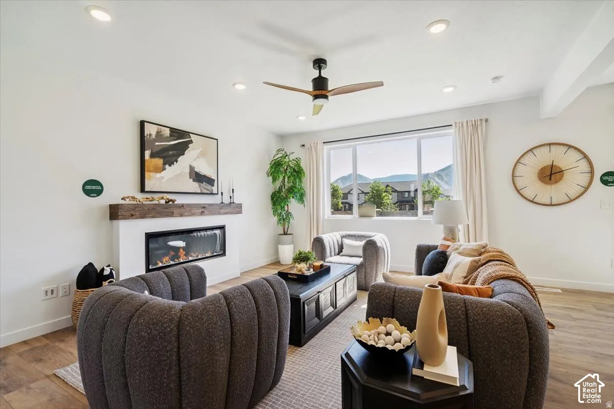 Living area with wood-finish flooring, a linear electric fireplace with a wood-beam mantel, recessed lighting, and a ceiling fan