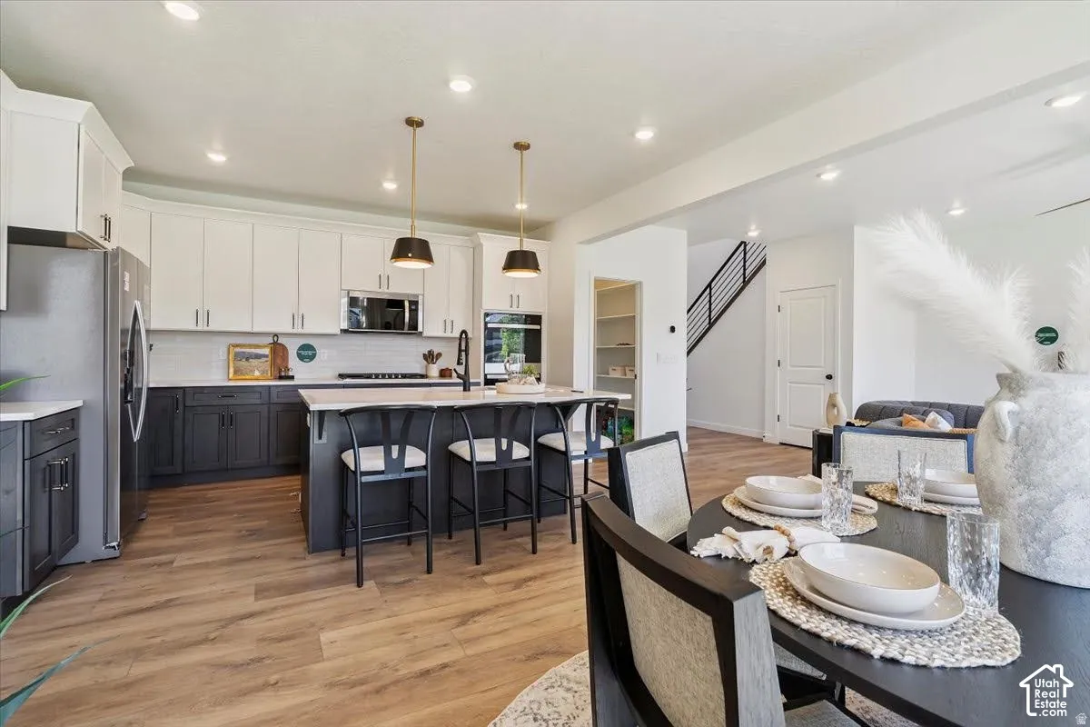 Open-concept kitchen with wood-finish flooring, two-tone cabinetry, stainless steel appliances, and a central island with pendant lighting