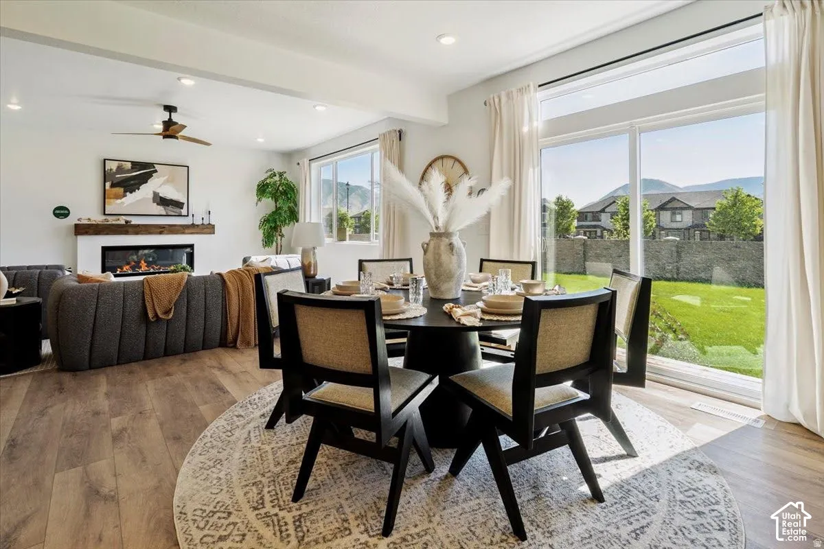 Spacious living area featuring wood-finish flooring, a linear fireplace with a wood mantel, and a ceiling fan with integrated lighting