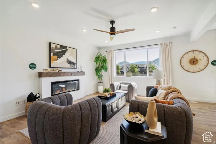 Living area with wood-finish flooring, a linear electric fireplace with a wood-beam mantel, recessed lighting, and a ceiling fan