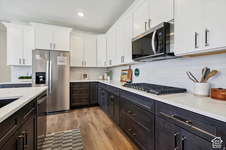 Contemporary kitchen featuring white shaker-style cabinetry with brushed nickel hardware, contrasting dark lower cabinets with full-extension drawers, quartz countertops, stainless steel appliances including a gas cooktop and built-in microwave, and wood-