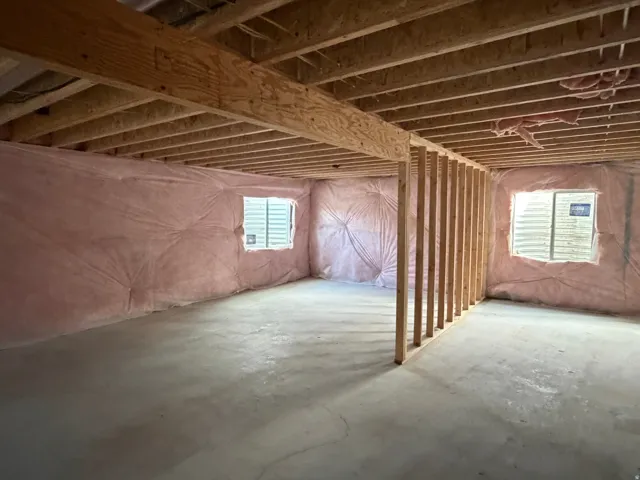 Unfinished basement space with exposed wooden joists, framed walls, two egress windows, and concrete flooring
