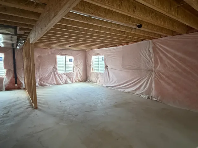 Unfinished basement with exposed wood joists, concrete flooring, insulated walls, and multiple windows