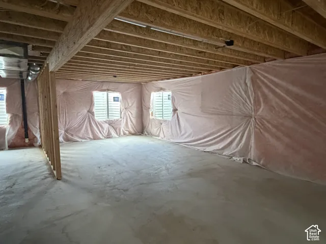 Unfinished basement with exposed wood joists, concrete flooring, insulated walls, and multiple windows