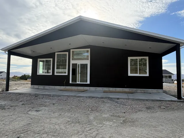 Contemporary exterior with dark stucco, white window frames, and a covered concrete patio