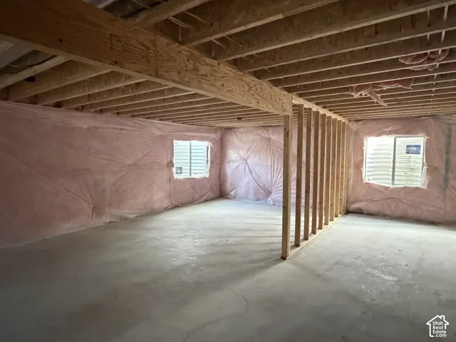 Unfinished basement space with exposed wooden joists, framed walls, two egress windows, and concrete flooring