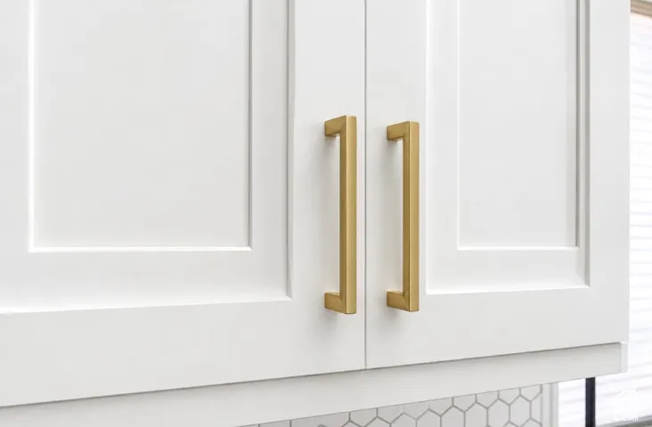 White shaker-style cabinetry with gold-tone hardware and hexagonal tile backsplash
