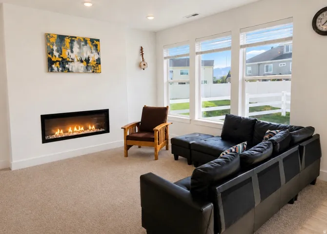Recessed linear fireplace, multiple large windows, flush-mount lighting, and neutral carpeting