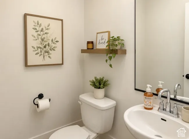 Pedestal sink with chrome faucet, a rectangular mirror with a black frame, and a floating wood-finish shelf