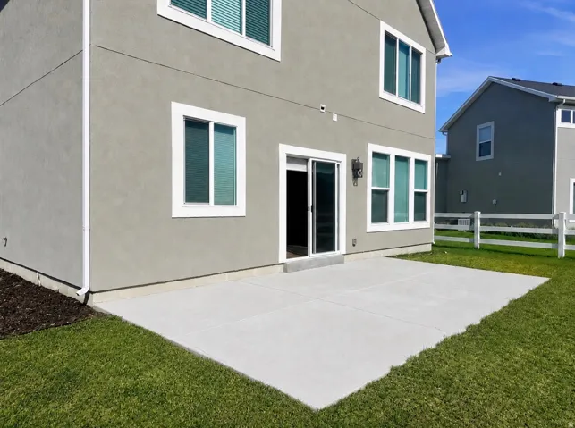 Expansive concrete patio with direct outdoor access, stucco exterior, white window frames, and a manicured lawn