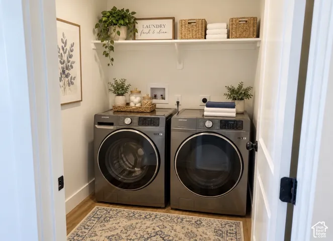 Laundry area featuring wood-finish flooring, a wall-mounted shelving unit, and plumbing hookups